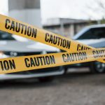 Black and white vehicles. Yellow caution tape near the car parking lot at daytime. Crime scene