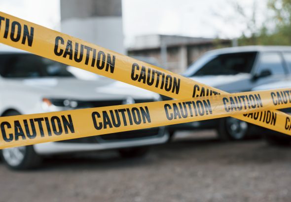 Black and white vehicles. Yellow caution tape near the car parking lot at daytime. Crime scene